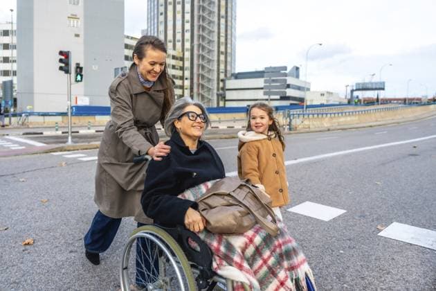 Familienmitglieder helfen einer älteren Frau im Rollstuhl im Freien, Enkelin, die beim Navigieren durch die Stadt nebenan geht und für Pflege, Unterstützung und einen aktiven Lebensstil älterer Menschen steht Family members assisting senior woman in wheelchair outdoors, granddaughter walking alongside while navigating city street, representing care, support, and active lifestyle for elderly Copyright: imageBROKER UnaixHuizi ibxuhu16530801.jpg ,model released, Symbolfoto ,property released