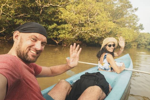Glückliches kaukasisches Touristenpaar sitzt im blauen Doppelkajak und winkt. Ein Paar Kajaks auf ruhigem Wasser, umgeben von üppigen Mangroven und tropischer Natur Happy caucasian tourist couple sit in double blue kayak and wave. Couple kayaks on calm waters surrounded by lush mangroves and tropical nature Copyright: imageBROKER EvaldasxMikoliunas ibxemi16699192.jpg ,model released, Symbolfoto ,property released