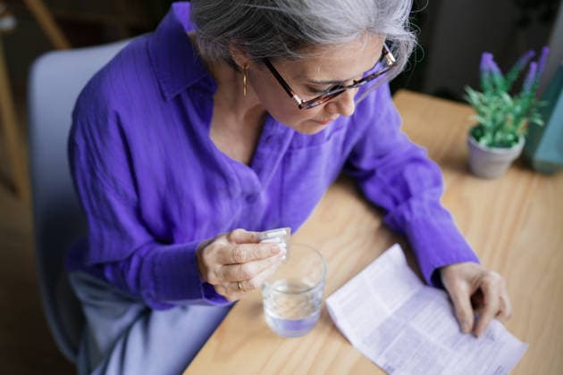 Woman reading instructions and taking medication at table indoors model released, Symbolfoto property released, ATSF00308