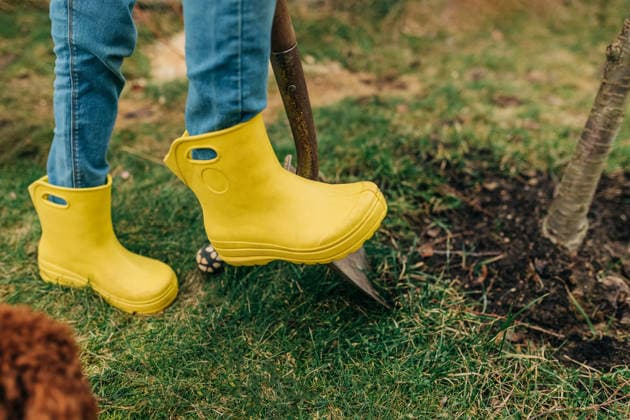 Person wearing yellow rubber boots digging soil in outdoor spring garden model released, Symbolfoto, NASF00115