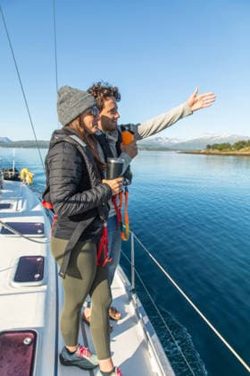 Couple enjoying a boat adventure in Norway A couple enjoys a serene boat trip on clear Norwegian waters. They are warmly dressed, taking in the stunning view of distant mountains on a sunny, peaceful day at sea. Model Released Robcabphotography_ID33004_1123786_045 Copyright: xRobcabphotographyx RECORD DATE NOT STATED