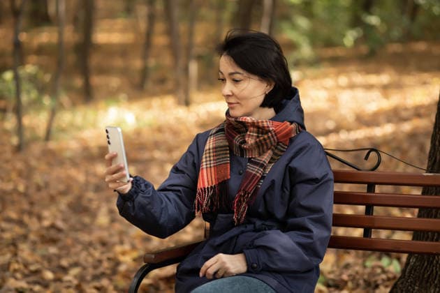 Woman enjoying autumn in park with smartphone Woman sitting on a park bench during autumn, holding a smartphone. Fallen leaves cover the ground, creating a warm, golden ambiance. The scene captures a peaceful, seasonal moment. Model Released ZulfiiaIshmukhametova_ID32598_1110457_006 Copyright: xZulfiiaxIshmukhametovax RECORD DATE NOT STATED