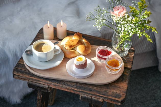 IMAGO Creative, Ostern, Bräuche, Osterbrunch Mit Liebe zubereitetes Frühstück auf einem alten rustikalen Holztisch vor dem Bett, Tablett mit Kaffee, Marmelade, Brötchen und Ei, dekoriert mit Kerzen und Blumen, ausgewählter Fokus Breakfast prepared with love on an old rustic wooden bedside table in front of the bed, tray with coffee, jam, bun and egg, decorated with candles and flowers, selected focus, narrow depth of field (License=RF) Copyright: xZoonar.com maren-winter.dex 24707183
