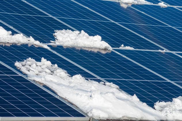 Im Winter sind die Solarmodule teilweise mit Schnee bedeckt, was sich auf die Energieeffizienz auswirkt. Snow partially covers a series of blue solar panels, affecting energy production in winter weather conditions. (License=RF) Copyright: xZoonar.com AndriixAbryutinx 24730274