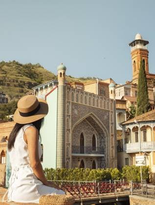 Frau sitzt im Sommerkleid mit Strohhut und bewundert die lebendige Architektur der Altstadt von Tiflis, Georgien. Traditionelle Holzbalkone, Moschee Minarett und historische Gebäude. Reisen, Sightseeing, Sommerurlaub Woman sit in summer dress straw hat admiring vibrant architecture old town Tbilisi, Georgia. Traditional wooden balconies, mosque minaret, and historic buildings. Travel, sightseeing, summer vacation Copyright: imageBROKER EvaldasxMikoliunas ibxemi16707968.jpg ,model released, Symbolfoto ,property released