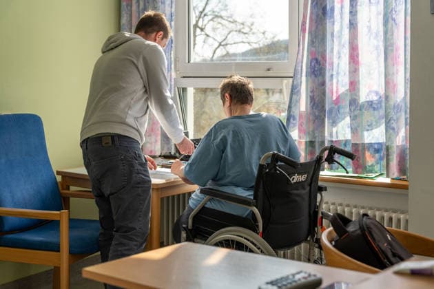 Bavaria, Germany - March 10, 2026: A caregiver assists a patient in a wheelchair with a task at a table in a care facility. The scene depicts everyday life in nursing care, where support, assistance, and human compassion play a central role.
