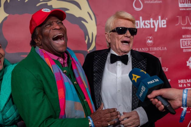 Datum: 13.03.26 Ort: Kitzbühel Im Bild: Roberto Blanco mit Heino Er ist Kult blonde Haare, schwarze Sonnenbrille und eine unverwechselbare Jahrhundertstimme: Heino (87) blickt auf eine fast 70-jährige Karriere zurück. Doch nur wenige kennen die Geschichte hinter seiner berühmten dunklen Brille. Der Sänger, der bürgerlich Heinz Georg Kramm heißt, hat in seinem Leben über 55 Millionen Tonträger verkauft. Ob Schlager, Pop, Heavy Metal, Ballermann, Rap oder Klassik kaum ein Genre blieb ihm fremd. Bis heute steht der Kultstar auf der Bühne: Er tritt bei großen Festivals wie dem Parookaville vor Zehntausenden Fans genauso selbstverständlich auf wie bei klassischen Kirchenkonzerten, etwa in der Dresdner Kreuzkirche, oder b xchristian esslerx