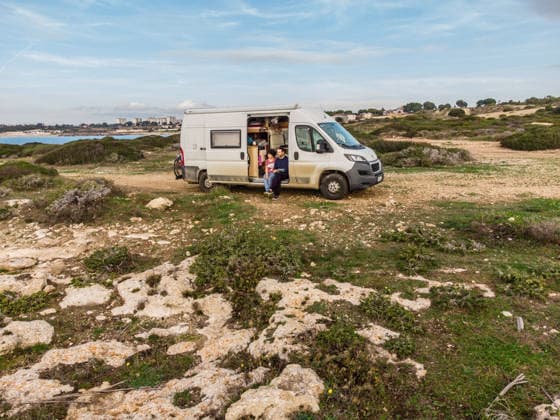 Camper sitzen in der Schiebetür ihres Campers auf einem unbefestigten Offroad Stellplatz an der Küste am Mittelmeer bei Tarent. Salento, Apulien, Italien. Ein Wohnmobil steht auf einem Schotterplatz am Ufer des Mittelmeers. *** Campers sit in the sliding door of their camper on an unpaved off-road pitch on the Mediterranean coast near Taranto Salento, Puglia, Italy A camper van is parked on a gravel pitch on the shore of the Mediterranean Sea