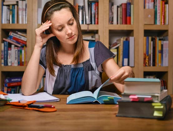 Woman reading books at a table in a library with shelves in the background. Germany Indoor, living room Germany mlma01199 Copyright: xConnectxImagesx ,model released ,property released
