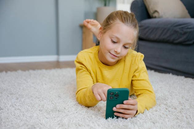 Child lying on carpet indoors using smartphone in living room model released, Symbolfoto property released, FLMZF03139