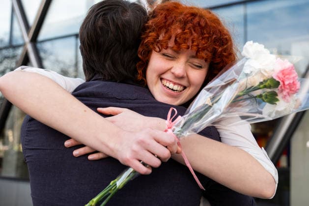 Redhead smiling while hugging partner with flowers outdoors in urban setting model released, Symbolfoto, CVMF00627