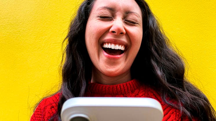 Laughing woman holding phone in front of yellow wall model released, Symbolfoto, AMWF03796