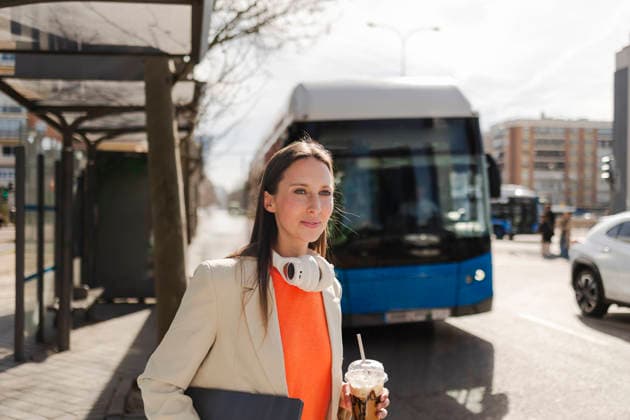 IMAGO Creative, Food, Trend, Iced Coffee Businesswoman with headphones and iced coffee waiting at urban bus stop model released, Symbolfoto, JCCMF14796
