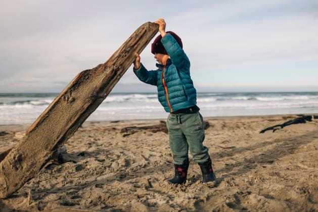 A young toddler picks up a log on a beach on a cold day. Manzanita, Oregon, United States CR_XICZ260323-1981041-01 ,model released, Symbolfoto