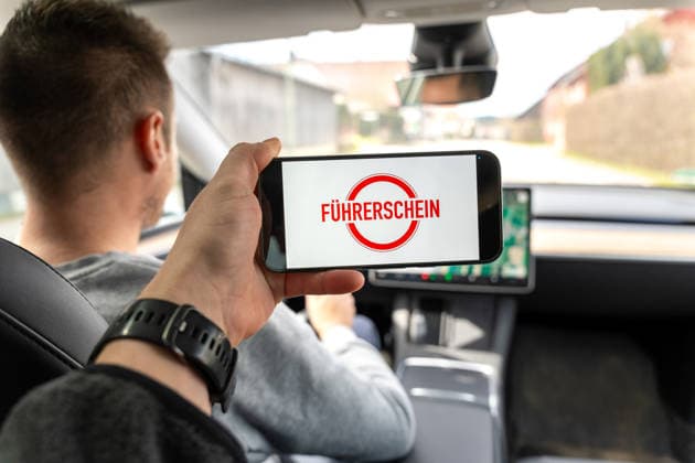 Bavaria, Allgäu, Germany April 5, 2026: A driver holds up a smartphone displaying the word driver™s license? and stands for changes in traffic law. The image symbolizes new rules, regulations, and adjustments related to driver™s licenses and traffic safety. *** Ein Autofahrer hält ein Smartphone mit dem Hinweis Führerschein und steht für Änderungen im Verkehrsrecht. Das Bild symbolisiert neue Regeln, Vorschriften und Anpassungen rund um Fahrerlaubnis und Verkehrssicherheit.