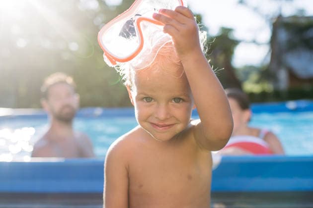 Smiling toddler boy putting on swimming goggles in backyard pool . Smiling toddler boy putting on swimming goggles in backyard pool on sunny day. model released