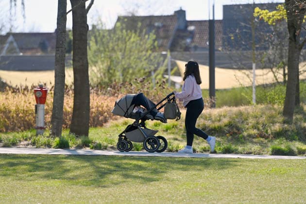 Frau schiebt Kinderwagen durch einen Park *** Woman pushing baby carriage through a park