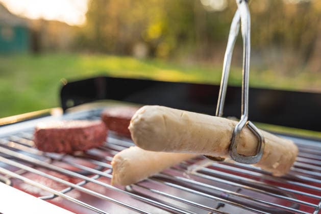 Bavaria, Germany April 7, 2026: During a springtime barbecue in the garden, tongs flip vegan sausages and plant-based steaks on the electric grill. Meat alternatives sit on the grill as an alternative to traditional barbecue fare *** Beim Grillen im Garten im Frühling wendet eine Zange vegane Bratwürste und pflanzliche Steaks auf dem Elektrogrill. Fleischersatzprodukte liegen als Alternative zu klassischem Grillgut auf dem Rost