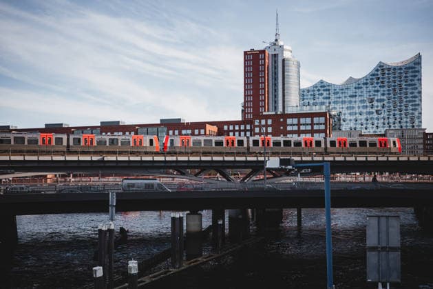 Deutschland, Hamburg U-Bahnlinie U3 auf der Elbbrücke, Hochbahnzug (DT5) im Linienbetrieb im Netz des Hamburger Verkehrsverbund (HVV), zentrale Achse zwischen Innenstadt und HafenCity; im Hintergrund Elbphilharmonie und Hanseatic Trade Center, Columbus-Haus, Standort von Taylor Wessing; darunter Straßenverkehr und Elbe. Kontext Mobilität: Hamburg-Takt als langfristige Strategie zum Ausbau des ÖPNV, nicht nur ein 5-Minuten-Takt-Ziel; umfasst Ausbau von U- und S-Bahnlinien, dichtere Taktung, optimierten Busverkehr, Integration des Deutschlandtickets sowie zukünftige Technologien wie autonomes Fahren; Anpassungen durch veränderte Nachfrage seit der Corona-Pandemie. Stadtentwicklung: steigende Fahrgastzahlen auf Vorkrisenniveau, Copyright: xStefanxTrochax
