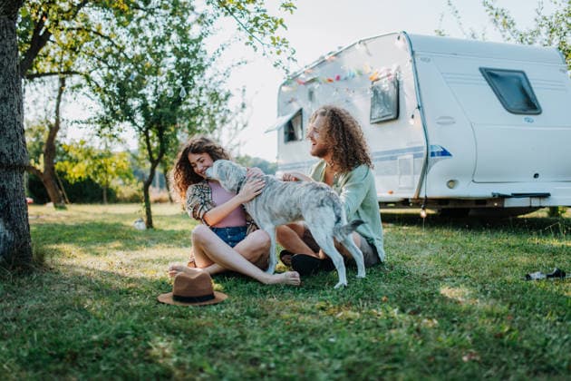 Young couple and dog are on a camping trip in nature, sitting in front of caravan. Caravan traveling for young people. Young couple and dog are on a camping trip in nature, sitting in front of caravan, camper. Caravan traveling for young people model released