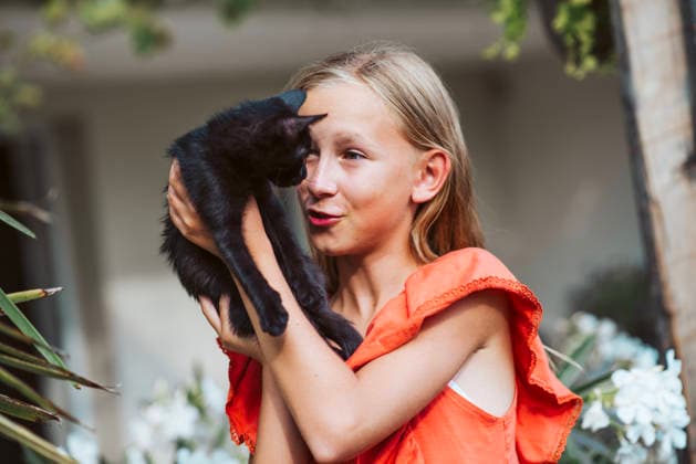 Girl holding black kitten and looking at it in garden. Girl holding black kitten and looking at it with care in garden. model released