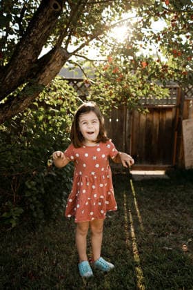 Young girl laughing in a sunlit backyard under a cherry tree Calgary, Alberta, Canada CR_AMST260410-1995950-01 ,model released, Symbolfoto ,property released