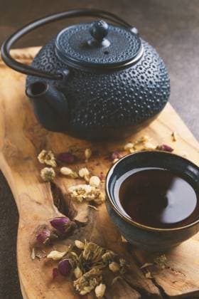 Eine gußeiserne Tetsubin Teekanne und eine Tasse Tee auf einem hölzernen Schneidebrett, Blumentee verteilt A cast-iron tetsubin teapot and a cup of tea, on a wooden chopping board, flower tea scattered around Copyright: imageBROKER GalinaxDidebashvili ibxggd17327288.jpg