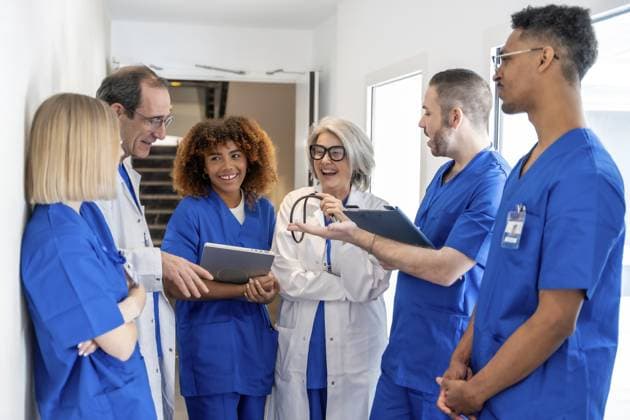 Vielfältige Gruppe von Ärzten und Krankenschwestern in Peelings und Laborkitteln, die in einem modernen Krankenhausflur eine lebhafte Diskussion führen, zusammenarbeiten und lächeln Diverse group of doctors and nurses wearing scrubs and lab coats engaging in a lively discussion, collaborating and smiling in a modern hospital hallway Copyright: imageBROKER UnaixHuizi ibluhu17150429.jpg ,model released, Symbolfoto ,property released