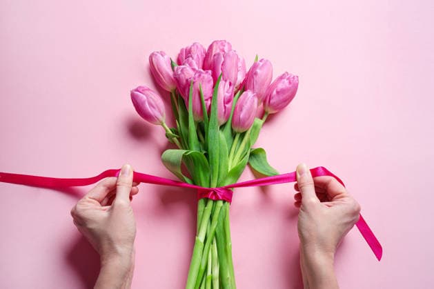 Eine Frau bindet eine rosa Schleife an Tulpen, Muttertag Woman hands tying pink ribbon on tulip bouquet on pink background, top view. Mother s Day, Valentine s Day or other holiday gift concept. (License=RF) Copyright: xZoonar.com OksanaxBratanovax 24867368