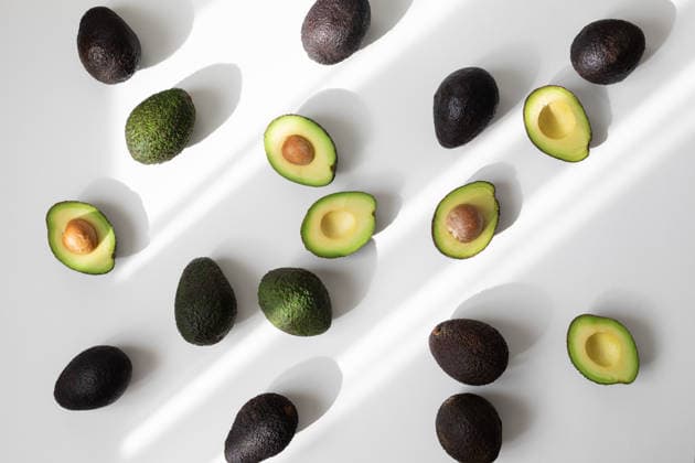 Ein Haufen reifer ganzer und halber Avocados auf weißem Hintergrund, von oben betrachtet, in ästhetischem Schattenlicht. Flat-Lay-Stil. Heap of ripe whole and half avocados on white background top view in aesthetic shadow sunlight. Flat lay style. (License=RF) Copyright: xZoonar.com JuliaxSudnitskayax 24875223
