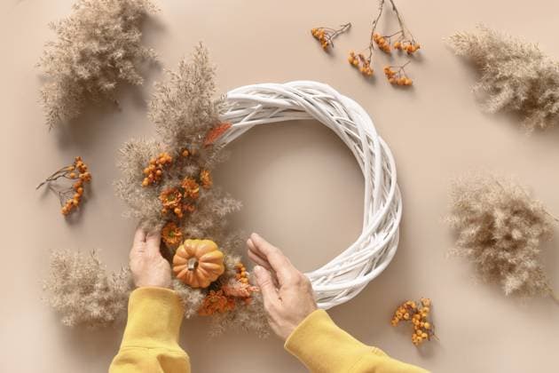 Frau bastelt einen Kranz mit orangefarbenen Blüten und trockenen Naturmaterialien auf beigem Hintergrund. Ansicht von oben. SELBERMACHEN. Workshop für handgemachte Dekoration zum Erntedankfest Woman making wreath with orange flowers and dry natural materials over beige background. Top view. DIY. Workshop for handmade Thanksgiving day decoration Copyright: imageBROKER SvetlanaxLazhko ibxiqx17290981.jpg