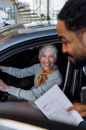 Smiling salesperson holding document near customer sitting in car model released, Symbolfoto property released, IKF01605