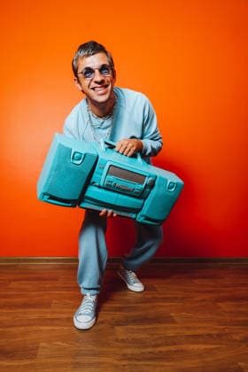 Smiling man with boombox in blue outfit posing against orange wall model released, Symbolfoto, AAF00275