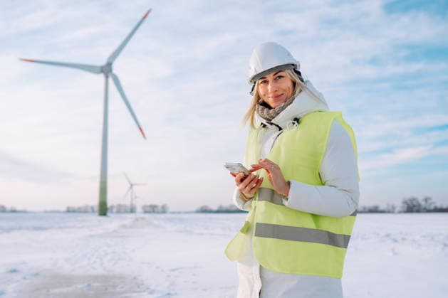 Smiling engineer holding smart phone standing at wind farm in winter model released, Symbolfoto, OLRF00185