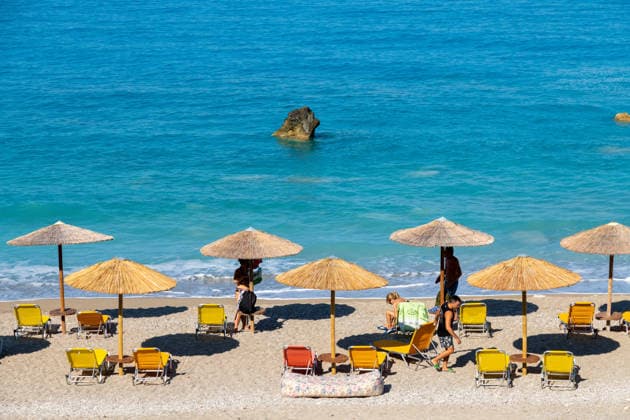 Sonnenschirme und Liegestühle mit Menschen am Meer Nydri - Ionian Islands - Greece - 08-09-2025: Beach scene with straw umbrellas, yellow and orange sunbeds, people relaxing on the sandy shore, and turquoise sea with visible rock. (License=RM) Copyright: xZoonar.com DetlefxVoigtxinfo@gph-foto.dex 24896723