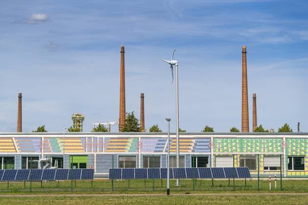 Solaranlagen und ein Windrad vor einem Gebäude der PCK Erdöl-Raffinerie Schwedt, hinten mehrere Schornsteine, Schwedt an der Oder, Uckermark, Brandenburg, Deutschland Solar systems and a wind turbine in front of a PCK Erdöl-Refinery Schwedt building, several chimneys in the back, Schwedt an der Oder, Uckermark, Brandenburg, Germany Copyright: imageBROKER OliverxGerhard ibloge17408824.jpg