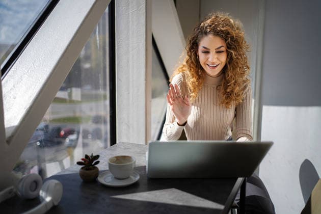 Frau, die während eines Videoanrufs über ihren Laptop in einem Café winkt Young adult woman smiling and waving at laptop screen during a video call (License=RF) ,model released, Symbolfoto Copyright: xZoonar.com JelenaxCvetkovicx 24957914 ,model released, Symbolfoto ,property released