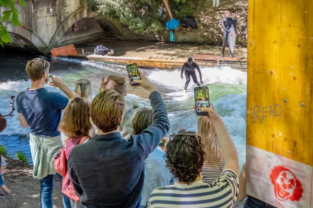 Die berühmte Surfwelle iläuft wieder! Surfer und Zuschauer an der Eisbachwelle am Samstagmittag, München, 2. Mai 2026 Deutschland, München, 2. Mai 2026, die berühmte Surfwelle läuft wieder! Surfer auf der Eisbachwelle am Samstagmittag, viele Münchner und Touristen säumen das Bachufer, filmen die Szenen mit ihrem Handy, alle freuen sich über die Rückkehr der Welle, die Surfwelle ist seit ein paar Tagen wie durch ein Wunder wieder da, Spekulation: durch höheren Wasserstand und eine bessere Strömung hat sich die perfekte Welle wohl von selbst wieder stabilisiert, es sind keine illegalen Einbauten bekannt, es gilt jedoch weiter das Surfverbot der Stadt, die Verbotsschilder sind übersprüht oder abgehängt, nicht mehr sichtbar, sc