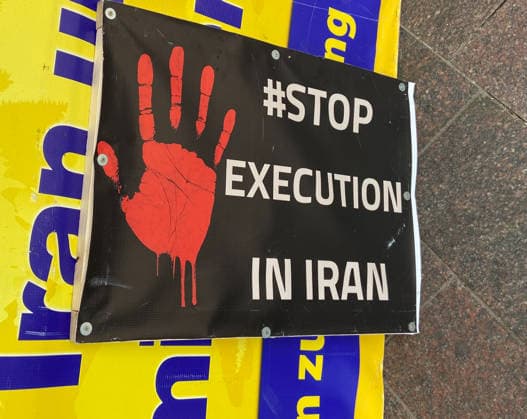 Flensburg, Schleswig Holstein A black protest poster with a red palm and the words STOP EXECUTION IN IRAN, attached in front of a yellow banner The imagery is clear, direct and designed for visual attention it refers to human rights violations, the death penalty and international protest Picture taken on 02 05 2026, Flensburg