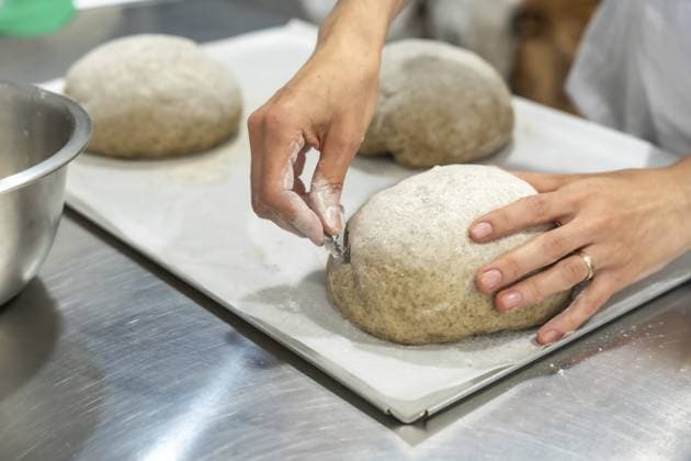 Bäckerhände ritzen ein rundes Sauerteigbrot mit einer scharfen Lahme auf Pergament, Nahaufnahme, die handwerkliche Technik zeigt und mit Mehl bestäubten Teig, fertig zum Backen in einer rustikalen Küche Baker s hands scoring round sourdough loaf with a sharp lame on parchment, close up showing artisan technique and flour dusted dough ready for baking in a rustic kitchen Copyright: imageBROKER UnaixHuizi ibxuhu17015826.jpg ,model released, Symbolfoto ,property released