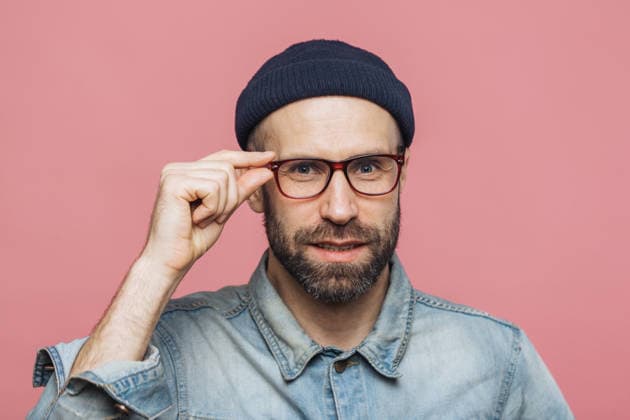 Neugieriger erwachsener Mann, der in einem Studio-Porträt vor rosa Hintergrund seine Brille zurechtrückt; er trägt ein Jeanshemd und eine dunkle Mütze Curious Adult Man Adjusting Eyeglasses in Studio Portrait on Pink Background Wearing Denim Shirt and Dark Beanie (License=RF) ,model released, Symbolfoto Copyright: xZoonar.com ViorelxKurnosovx 25041930 ,model released, Symbolfoto ,property released
