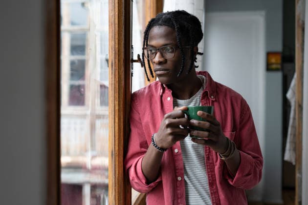 Ein einsamer, trauriger Afroamerikaner, der eine Tasse Tee in der Hand hält, aus dem Fenster schaut und drinnen steht Lonely sad African man looking out window standing indoors suffering due to separation from girlfriend or lack of friends. Unhappy young black guy in casual clothes holding mug with tea or coffee (License=RF) ,model released, Symbolfoto Copyright: xZoonar.com DmitriixMarchenkox xEnvatox 25042202 ,model released, Symbolfoto ,property released