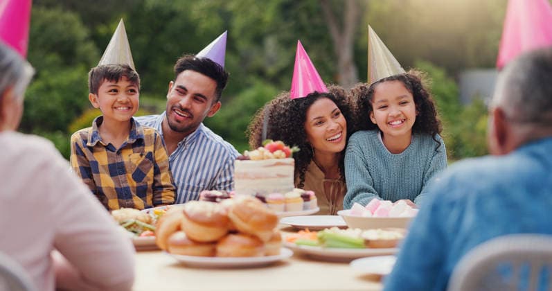 Parents, children and happy with birthday cake in garden with care, love and bonding with food at family home. Father, mother and kids with hat for party, event and embrace at table with celebration. (License=RF) ,model released, Symbolfoto  Copyright: xZoonar.com KasperxRavlox 21563318 ,model released, Symbolfoto ,property released
