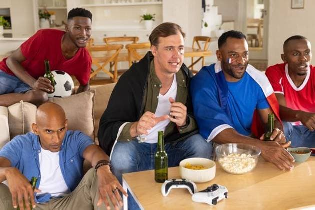 Diverse male friends watching key play on screen at home leaning, reaching popcorn and soccer ball, model released, property released, Cape Town, South Africa, 18.03.2026 06:00:00, 12882363 Copyright: xIS-260416xcreatorid:x393x 12882363