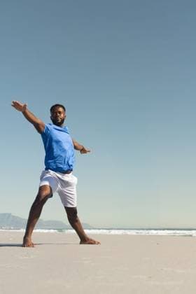 African American man standing barefoot on sandy beach at waterline wearing blue shirt white shorts, model released, property released, 27.03.2025 06:00:00, 12885004 Copyright: xIMS-260410_1xcreatorid:x331x 12885004