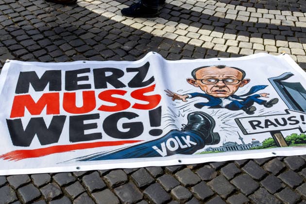 Augsburg, Bavaria, Germany May 16, 2026: Demonstration in Augsburg against the current federal government led by Chancellor Friedrich Merz. Under the slogan: Merz must go! Banner with the inscription: MERZ MUST GO! Featuring an illustration of a foot standing on the word PEOPLE and an illustration of Chancellor Friedrich Merz (CDU) flying through a door with a sign reading: GET OUT! *** Demonstration gegen die aktuelle Bundesregierung unter Bundeskanzler Friedrich Merz in Augsburg. Unter dem Motto: Merz muss weg! Banner mit Aufschrift: MERZ MUSS WEG! Mit Illustration von einem Fuß auf dem VOLK steht und einer Illustration von Bundeskanzler Friedrich Merz (CDU) der durch eine Tür fliegt mit einem Schild mit Aufschrift: RAUS!