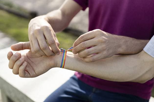 Nahaufnahme von zwei Männern, die ein Regenbogenbandarmband an ein Handgelenk binden, das LGBTQ+ Liebe, Stolz und Unterstützung symbolisiert Close-up of two men tying a rainbow ribbon bracelet on a wrist, symbolizing lgbtq+ love, pride, and support Copyright: imageBROKER AndresxVictorero ibxiqx17672330.jpg ,model released, Symbolfoto ,property released