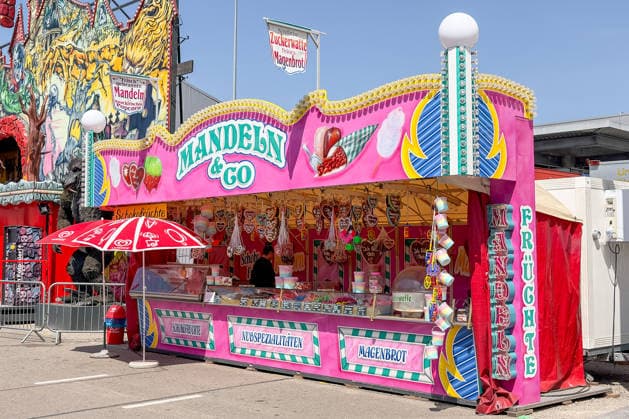 Freiburg im Breisgau GER, Volksfest, Freiburg im Breisgau, 24.05.2026 Ein bunter Süßwarenstand mit der Aufschrift Mandeln & Co bietet Schokofrüchte, Nussspezialitäten und Magenbrot auf einem Jahrmarkt an. Im Hintergrund ist eine Jahrmarktattraktion mit gruseligen Motiven zu erkennen. *** Freiburg im Breisgau GER, Volksfest, Freiburg im Breisgau, 24 05 2026 A colorful confectionery stand with the inscription Mandeln Co offers chocolate fruits, nut specialties and stomach bread at a fairground In the background you can see a fairground attraction with creepy motifs Copyright: xEibner-Pressefoto ThomasxHessx