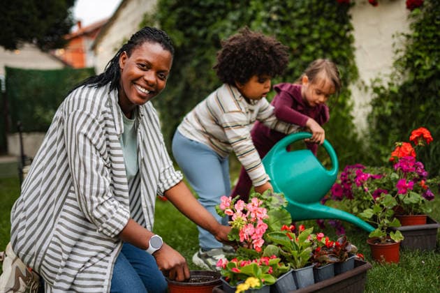 Mutter und Kinder pflanzen Blumen im Garten hinter dem Haus Smiling woman and two kids working together in garden, planting and watering flowers (License=RF) ,model released, Symbolfoto Copyright: xZoonar.com JelenaxCvetkovicx 25079957 ,model released, Symbolfoto ,property released