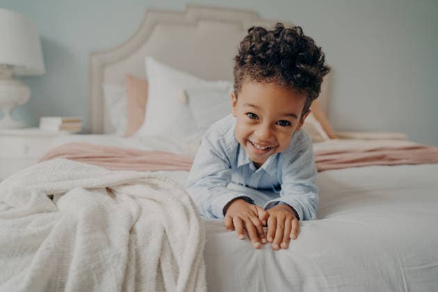 Ein fröhlicher afroamerikanischer Junge mit Locken, der auf dem Bett liegt und in die Kamera lächelt Portrait of happy curly mulatto boy smiling at camera while laying on cozy bed, relaxing after fun playing session at home, adorable preschool child enjoying indoor activities and leisure time (License=RF) ,model released, Symbolfoto Copyright: xZoonar.com ViorelxKurnosovx 25102261 ,model released, Symbolfoto ,property released